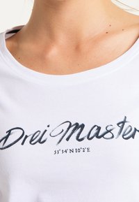 Camiseta de algodón blanca con cuello redondo. El diseño frontal incluye "Drei Master" en cursiva con las coordenadas impresas debajo en negro y gris.