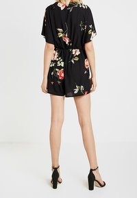 Mono corto negro con flores, mangas cortas, cintura elástica y un patrón floral con rosas. Combinado con zapatos de tacón negros.
