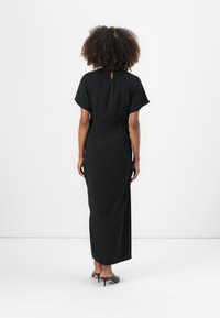 Black, floor-length dress with short sleeves and a keyhole back detail, made of smooth fabric, paired with high-heeled shoes.