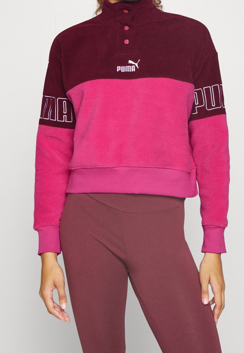 Femme portant un pull polaire bicolore rose et marron Puma avec col boutonné et leggings marron assortis.