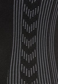 Zwarte stof met een textuurpatroon van witte stippen en pijlen, waardoor verticale lijnen ontstaan. Het patroon is gedetailleerd en gelijkmatig verdeeld over het oppervlak.