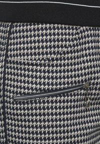 Houndstooth-patterned fabric in navy, white, and tan, featuring a zippered pocket and a black waistband with white stripes.
