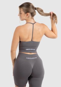 Ensemble de sport gris comprenant un crop top ajusté avec des fines bretelles et un short de vélo taille haute. Les deux pièces affichent des logos de marque bien visibles.