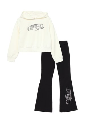 Felpa bianca corta con stampa nera "DIMENSIONE danza sisters", abbinata a leggings neri a zampa d'elefante con lo stesso logo in bianco.