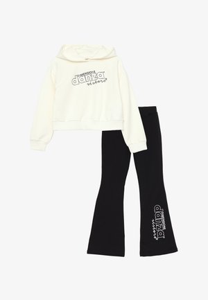 Felpa bianca corta con stampa nera "DIMENSIONE danza sisters", abbinata a leggings neri a zampa d'elefante con lo stesso logo in bianco.