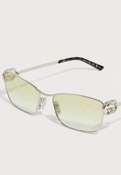 Ορθογώνια γυαλιά ηλίου με ασημί πλαίσιο και φακούς με κίτρινη απόχρωση, με το λογότυπο Gucci στα κλασικά μέρη και άκρα ναυτίλου στα πλάγια.