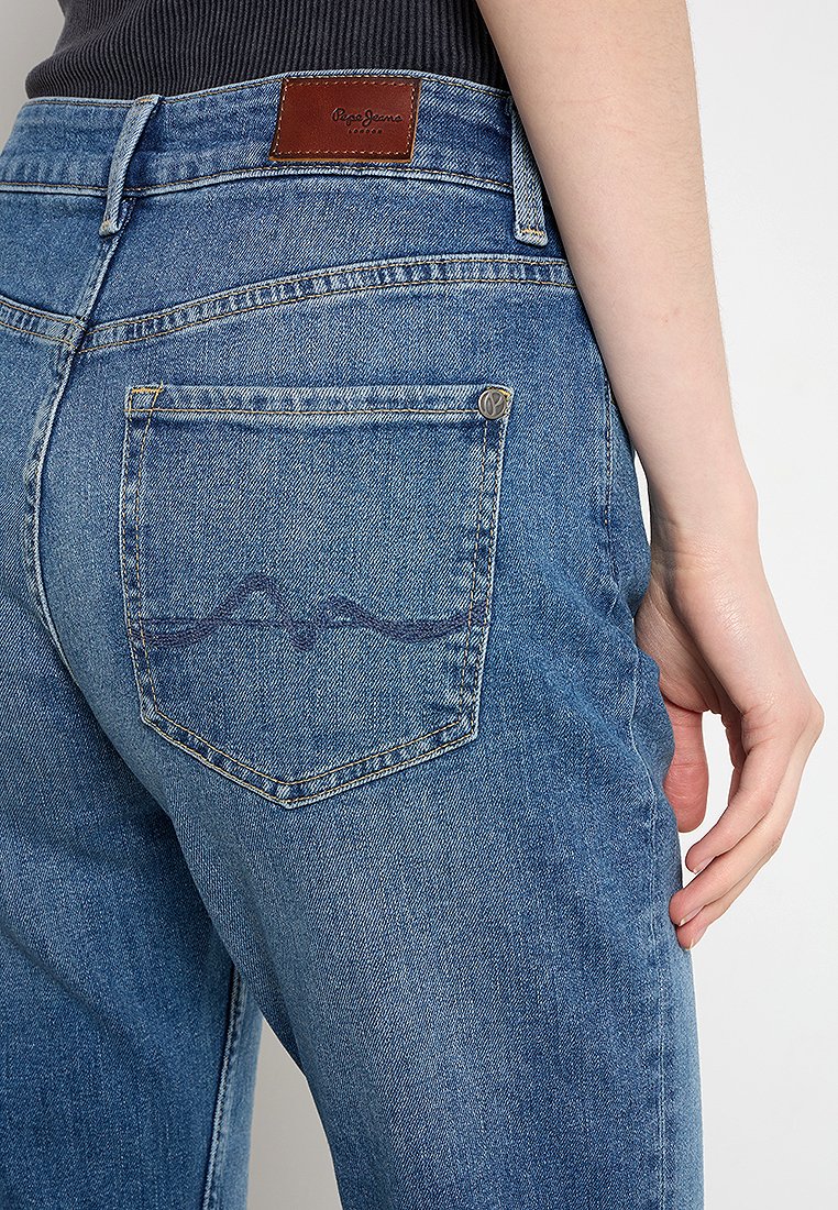 Helle blaue Denim-Jeans mit einer Gesäßtasche mit Wellenmuster und einem braunen Lederlabel. Enganliegendes Design, das von der Taille abwärts sichtbar ist.