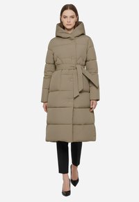 Cappotto imbottito verde oliva, con cappuccio, cintura in vita e texture trapuntata, caratterizzato da grandi quadrati e una silhouette dritta.