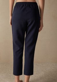 Pantaloni elasticizzati blu navy con cintura elastica. Lunghezza alla caviglia, texture liscia, con dettaglio della tasca posteriore.