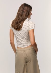 White short-sleeve crop top with black polka dots, featuring puff sleeves and a fitted design. Paired with beige elastic-waist cargo pants.