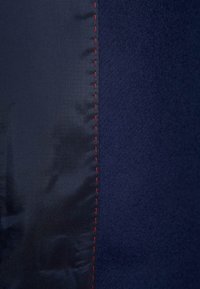 Panel z námořnicky modré látky s hladkou saténovou texturou vlevo a měkkou kartáčovanou texturou vpravo, rozdělený kontrastním červeným šitím.