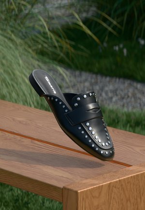 Scarpa nera in pelle slip-on con accenti borchiati e una fascia sopra il collo del piede. Texture liscia con design a punta.