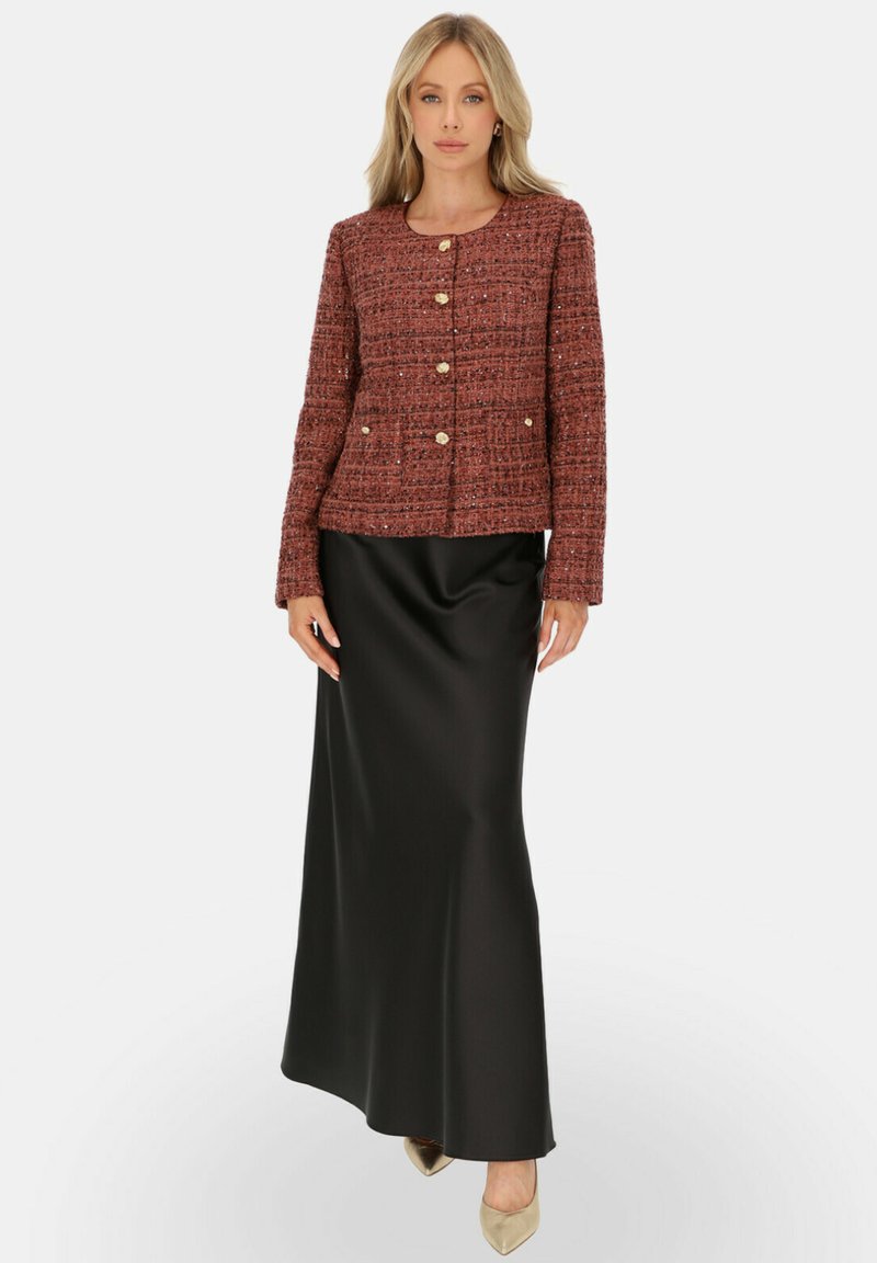Czerwona teksturowana kurtka z złotymi guzikami, połączona z czarną satynową długą spódnicą. Strój ma kwadratowy dekolt i długie rękawy.
