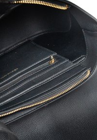 Czarna skórzana torebka na ramię z zamkiem błyskawicznym, kilkoma wewnętrznymi kieszeniami oraz fakturowaną powierzchnią z akcentami w odcieniu złota.