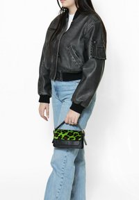 Geknipte zwarte leren bomberjack, slimfit manchetten, gecombineerd met lichtblauwe high-waisted jeans en een kleine zwarte handtas met groene luipaardprint.