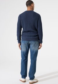 Marineblauwe geribbelde gebreide trui met lange mouwen en ronde hals, gecombineerd met lichtblauwe rechte jeans en witte sneakers.