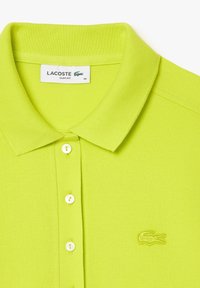 Koszulka polo Lacoste w wąskim kroju w jasnym limonkowym kolorze. Posiada klasyczny kołnierzyk, trzy guziki z przodu oraz haftowane logo na piersi.