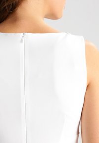 Weißes ärmelloses Kleid mit quadratischem Ausschnitt, glatter Textur und verborgenem Reißverschluss auf der Rückseite zum Verschließen.
