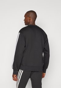 Sweatshirt preto com mangas longas, decote redondo e riscas brancas nas laterais. Feito de um material macio, com um corte relaxado e punhos canelados.