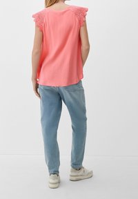 Haut sans manches corail avec des accents en dentelle festonnée sur les épaules, associé à un jean ample bleu clair et des baskets blanches.