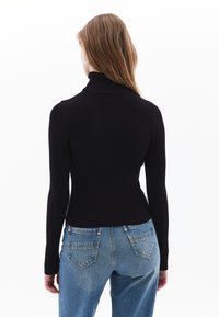 Schwarzer gerippter Rollkragenpullover mit einer taillierten Passform, langen Ärmeln und hohem Kragen; kombiniert mit hellblauen hochsitzenden Jeans.