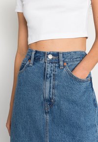 Denimkjol i ljusblått, midilengd, högmidjad med rak skärning. Har framfickor och synliga orangea sömdetaljer.