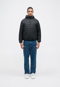 Quilted black puffer jacket with a hood, featuring a zip closure and side pockets, paired with blue denim wide-leg pants and white sneakers.