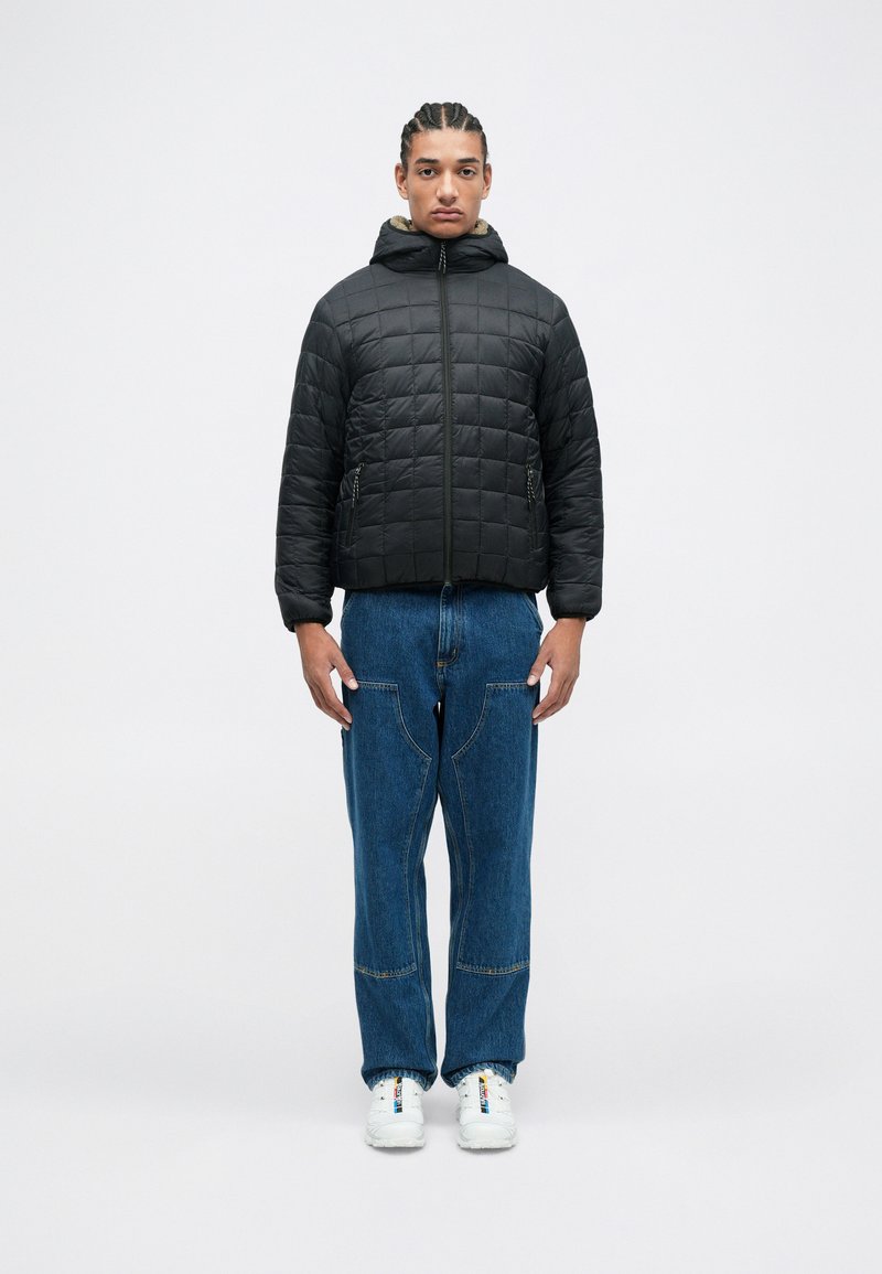 Quilted black puffer jacket with a hood, featuring a zip closure and side pockets, paired with blue denim wide-leg pants and white sneakers.