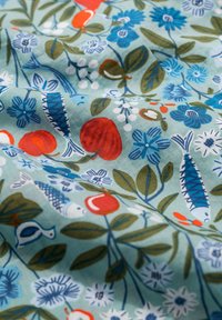 Tissu en coton avec un motif floral et de poissons. Les couleurs incluent le bleu, le rouge, le vert et le blanc sur un fond bleu clair avec des textures variées.