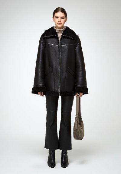 Crna kožna oversized jakna s kragnom od ovčje kože, s prednjim zatvaračem i bočnim džepovima, u kombinaciji s crnim kožnim hlačama s flared krojem.