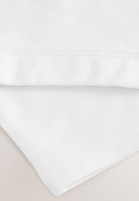 Gros plan sur un tissu blanc plié avec des détails de couture visibles sur une surface lisse.