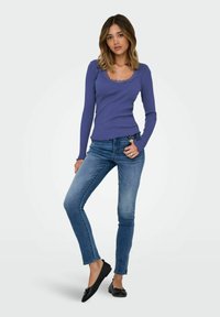 Långärmad lila ribbad topp med scallopkrage, kombinerad med blå skinnyjeans och svarta balettpumps. Slät textur, figurnära design.