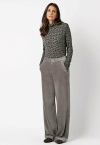 Langärmliges, eng anliegendes Rollkragentop aus dunklem, gemustertem Stoff kombiniert mit hoch taillierter, weit geschnittener grauer Cordhose mit seitlichen Taschen.