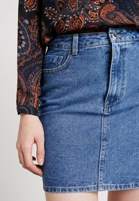 Falda de mezclilla en azul claro con un diseño ajustado, bolsillos frontales y un ligero desvanecimiento; combinada con una blusa de manga larga con estampado.