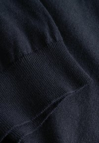 Sötét tengerészkék pulóver anyaga finom kötési textúrával és bordás mandzsetta részletekkel; puha, sima megjelenés, enyhe fényességgel.