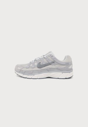 Chaussure de course Nike gris clair avec empiècements en mesh et en suède, semelle blanche épaisse et logo Swoosh sur le côté, présentée de profil sur un fond uni.