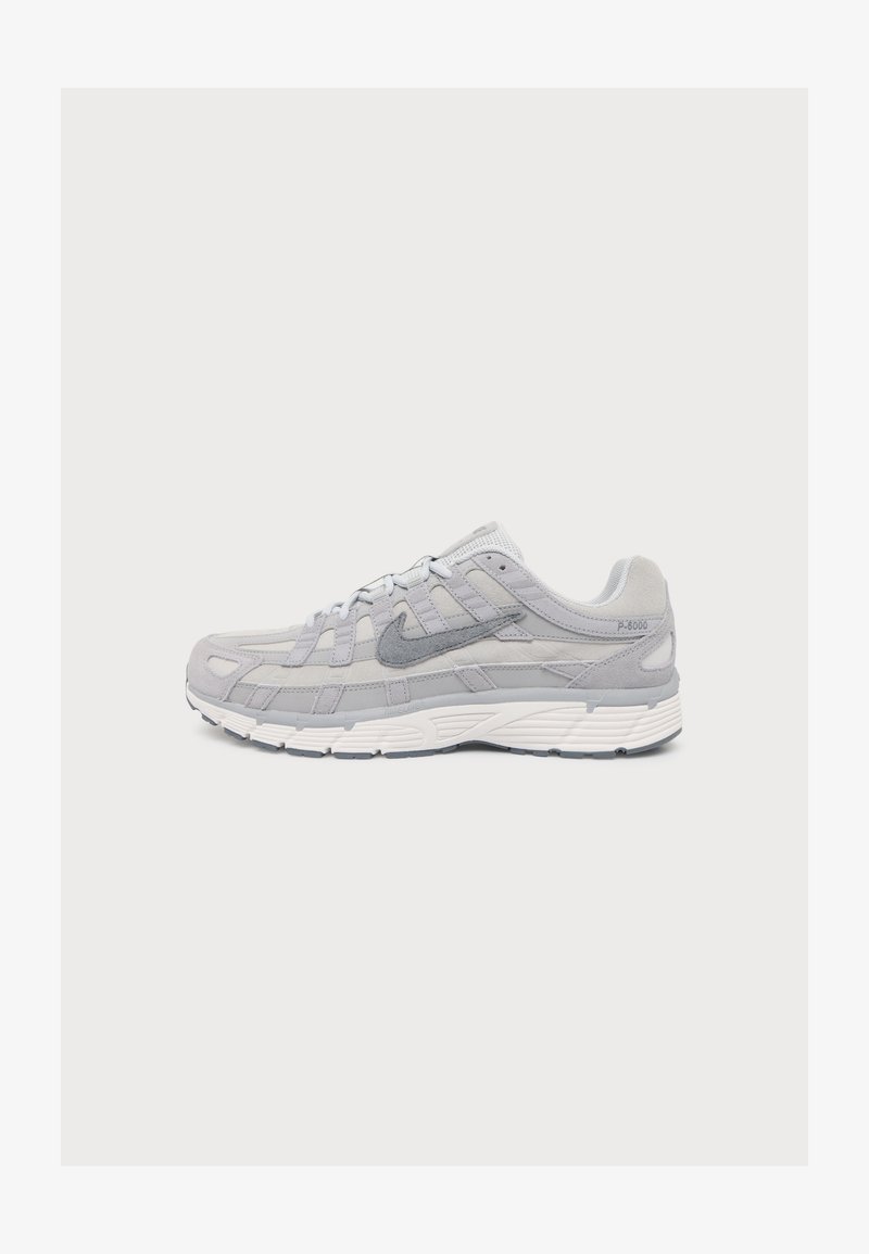 Ανοιχτό γκρι αθλητικό παπούτσι Nike με πάνελ από δίχτυ και σουέτ, χοντρή λευκή σόλα και πλάγιο λογότυπο Swoosh, εμφανίζεται προφίλ σε απλό φόντο.