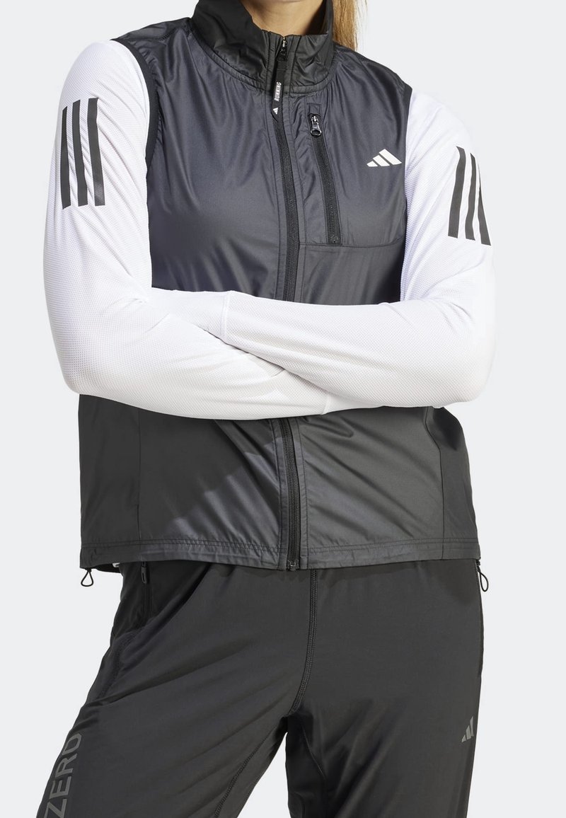 Czarna i biała kurtka sportowa z zamkiem na przodzie, wysokim kołnierzem i trzema czarnymi paskami na każdym rękawie. Wykonana z lekkiego, teksturowanego materiału.
