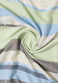 Textielstof in strepen van groen, blauw, grijs en wit. Bevat gestructureerde patronen met tekstaccenten in blauw en zwart die door het geheel geweven zijn.