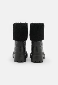 Czarne skórzane buty z grubym czarnym futrem syntetycznym na mankiecie, wytrzymałą podeszwą i bocznymi detalami. Projekt jest prosty i solidny, bez ozdobników.