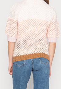 Sweter dziergany o teksturowanym, otwartym designie; gradient od różowego przez brzoskwiniowy do brązowego; ściągacze na rękawach i u dołu; noszony z niebieskimi dżinsami.