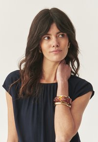 Set di bangles che presenta un bracciale traslucido di colore ambra con dettagli dorati. Il modello indossa una blusa blu navy con maniche corte e morbide.