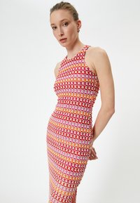 Enganliegendes Kleid mit ärmellosem Design und einem sich wiederholenden Wellenmuster in Rot, Pink, Orange und Creme; strukturierter Strickstoff.