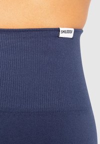 Marineblauwe high-waisted leggings gemaakt van een geribbelde stof, met een klein wit label met "SMILODOX" geborduurd op de taille.