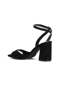 Sandalias de tacón de ante negro con punta abierta, tira en el tobillo y tacón grueso. Textura suave con un diseño curvado y acentos mínimos.