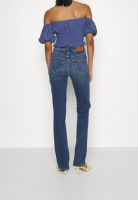 Modrá off-shoulder blůza s nabíranými rukávy, spárovaná s úzkými tmavě modrými džíny se zadními kapsami a koženou značkovou nášivkou.