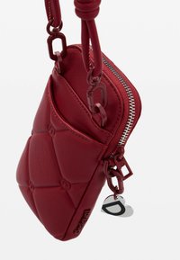 Rote Leder-Crossbody-Tasche mit gestepptem Design, silbernen Reißverschlussdetails und Kettenakzenten. Mit einem herzförmigen Anhänger mit einem 'D'-Logo.
