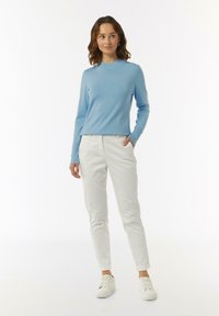Lichtblauwe gebreide trui met een ronde halslijn, gecombineerd met witte slim-fit broeken en witte sneakers. Gladde textuur, casual ontwerp.