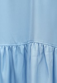 Svetlomodrá látka s hladkou textúrou má detail volánového lemu, ktorý vytvára plynulý siluetu. Jednoduchý a elegantný dizajn.