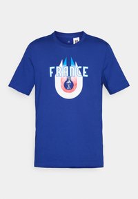 Zils kokvilnas T-krekls ar vārdu "FRANCIJA" baltā krāsā, zem kura ir apļa grafika, kas attēlo futbolu un logotipu sarkanā un zilā krāsā.